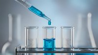 Laboratory pipette dropping blue chemical solution into glass test tube during scientific research experiment in modern lab setting.