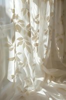 Elegant cream curtains with botanical leaf pattern filtering soft natural light through window creating gentle shadows and peaceful home interior atmosphere.