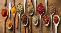 Colorful spices and herbs arranged in wooden spoons on rustic wood background. Culinary ingredients for cooking and seasoning food preparation.