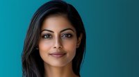Young South Asian woman with long dark hair and radiant smile against turquoise background, professional headshot style portrait showcasing natural beauty and confidence.