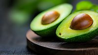 Fresh ripe avocado cut in half showing brown pit on dark wooden board against black background. Close up view with selective focus and copy space.