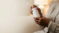 Senior woman with dark skin tone holding white cosmetic jar, wearing beige knit sweater. Skincare product mockup for beauty and wellness marketing.