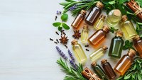 Natural essential oil bottles with fresh herbs and spices on white wooden background for aromatherapy and wellness treatments.