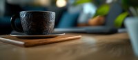 Dark ceramic cup with ornate pattern on wooden table against blurred background, moody atmospheric lighting creates cozy morning ambiance.