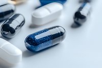 Macro view of blue and white medical capsules and pills scattered on light surface. Pharmaceutical and healthcare concept showing medicine dosage.