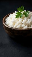 Cooked white rice in wooden bowl garnished with fresh parsley on dark slate background for culinary and food photography projects.