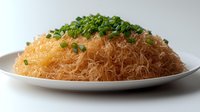 Crispy golden kataifi pastry strands garnished with fresh chopped chives on white ceramic plate, close-up view showing delicate texture and contrast of colors.