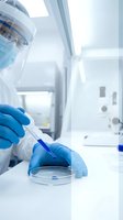 Laboratory scientist in protective gear conducting research with pipette and petri dish in sterile medical facility for pharmaceutical development.