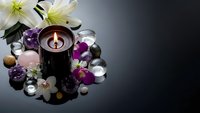 Spa wellness composition with burning candle, white lilies, purple orchids and healing crystals on dark reflective surface for relaxation therapy.