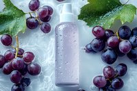 Fresh purple grapes with water drops surrounding cosmetic bottle on light background, natural skincare concept with grape extract for beauty product packaging.