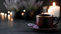 Dark ceramic cup with hot beverage on black surface against blurred candlelight background with lavender sprig creating cozy atmospheric composition.