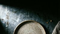 Uncooked quinoa in ceramic bowl on dark textured surface, overhead view for food styling and culinary content.