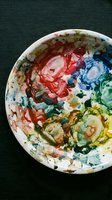 Artist's ceramic palette with vibrant acrylic paint in red, blue, yellow, and green hues mixed on white dish. Overhead view suitable for art education, creative workshops, and design projects.