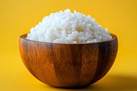 Steamed white rice in wooden bowl against vibrant yellow background, showcasing Asian cuisine staple for food blogs and restaurant menus.