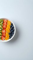 Colorful fruit bowl with kiwi, strawberry, orange and blueberry slices arranged in white ceramic dish on light background for healthy eating and nutrition content.