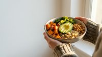 Healthy Buddha bowl with quinoa, roasted sweet potato, avocado and broccoli held in hands. Nutritious vegetarian meal for wellness lifestyle.