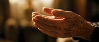 Elderly hands cupped in prayer or meditation gesture with warm golden light, representing spirituality, faith, hope, and peaceful contemplation.