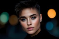 Close up portrait of young androgynous model with short dark hair and striking blue eyes against blurred city lights background, dramatic mood and lighting.