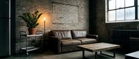 Loft-style living room with brown leather sofa, industrial metal shelving, potted plant, floor lamp, and wooden coffee table against exposed brick wall with window.