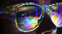 Vibrant rainbow light reflections on eyeglasses lens create prismatic effect against dark background, capturing iridescent spectrum and optical distortion in macro photography.