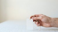 Caucasian male hand holding blank white tea bag with string against neutral background, suitable for beverage packaging, product mockups, and wellness marketing materials.