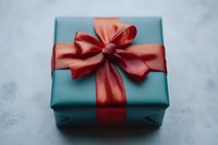 Elegant gift box wrapped in teal paper with luxurious coral red satin ribbon and bow on textured gray background, creating festive holiday mood.