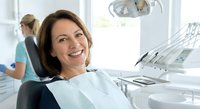 Middle-aged Caucasian woman smiling during dental appointment in modern clinic. Patient relaxing in dentist chair with professional equipment visible.