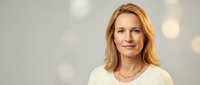 Professional blonde Caucasian businesswoman in cream sweater smiling confidently against soft bokeh background for corporate marketing materials.