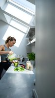 Young Caucasian woman making green smoothie in modern kitchen with skylights. Healthy lifestyle and nutrition concept for wellness content.