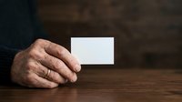 Senior male hand holding blank white business card on wooden table surface for corporate branding mockup.