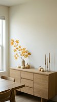 Modern minimalist dining room with wooden sideboard, autumn maple branch in vase, decorative pumpkins and brass candlesticks for seasonal home decor styling.