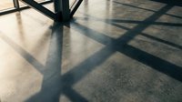 Dramatic shadows cast by metal railings create geometric patterns on polished concrete floor in modern architectural interior space.