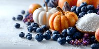 Seasonal autumn food composition with mini pumpkins, fresh blueberries, coconut flakes and dried fruits on light background.