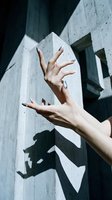Two female hands with manicured nails gesturing expressively against concrete architectural background with dramatic shadows for creative, editorial, and lifestyle projects.