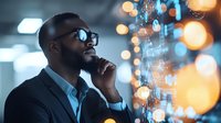 Young African American businessman in glasses talking on phone against blurred bokeh lights and digital data visualization background, contemplative expression.