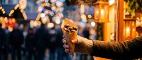Hand holding warm beverage cup at festive evening market with glowing lanterns and colorful bokeh lights creating cozy winter atmosphere for seasonal celebrations.