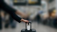 Businesswoman hand placing ballot into voting box at airport terminal with blurred crowd background for election concept.