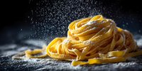 Fresh homemade pasta nest with flour dusting against dark background, showcasing traditional Italian cuisine preparation.