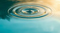 Water drop creating perfect ripples on calm turquoise surface with golden light reflection. Serene aquatic moment capturing fluid motion and tranquil atmosphere.