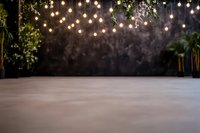 Empty event space with string lights hanging from greenery against dark backdrop, creating atmospheric ambiance for weddings or celebrations.