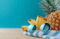 Summer vacation concept with fresh pineapple, sunglasses and striped towel on sandy beach against bright turquoise background for travel designs.