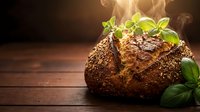 Fresh baked artisan bread with herbs and seeds on rustic wooden table with steam rising, perfect for bakery marketing and culinary content.