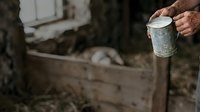 Male worker holding weathered metal paint can on construction site with wooden crate and blurred industrial background, suitable for labor and trades content.