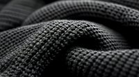Macro shot of black textured fabric with wavy folds creating abstract pattern. Detailed view of woven textile material showing geometric structure and depth in monochrome.