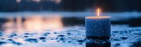Glowing candle with decorative snowflake pattern against blurred winter lake background at dusk creates peaceful seasonal atmosphere.