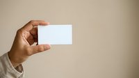 Man with medium skin tone holding blank white business card against neutral beige background, suitable for corporate branding, marketing materials, and professional presentations.