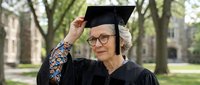 Mature Caucasian woman in graduation cap and gown celebrating academic achievement on university campus. Senior student graduate smiling with pride outdoors.