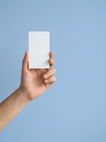 Male hand holding blank white card against blue background for branding, business card mockup, or promotional material display.