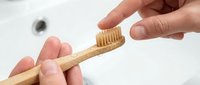 Hands holding eco-friendly bamboo toothbrush over white bathroom sink for sustainable oral hygiene and zero waste dental care routine.