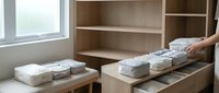 Woman organizing folded clothes in modern wooden wardrobe with open shelves and drawers. Home storage solution for bedroom closet organization.